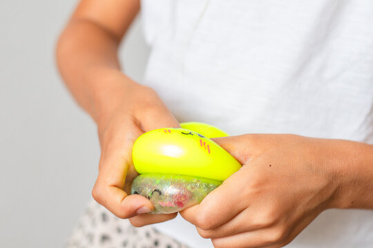 Child with light skin squeezing colorful squishy toy in hands, showcasing bright yellow and green colors against a neutral background