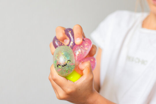Colorful collection of squishy toys held in child's hand, featuring various shapes and textures, with a soft background and playful design elements visible