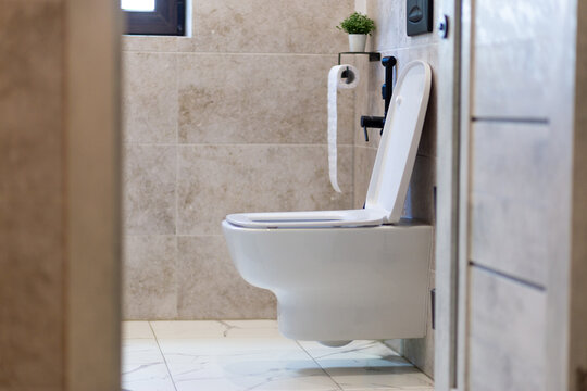 White toilet in a tiled bathroom at home, clean hygiene space, modern interior, household plumbing, simple bathroom design.