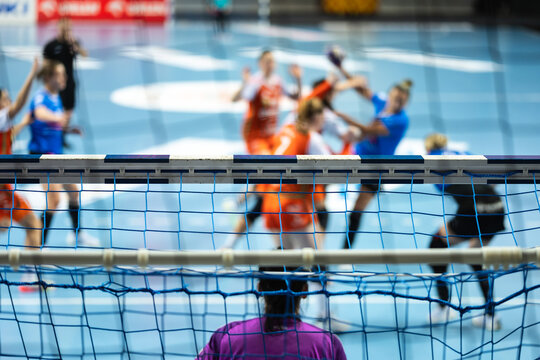 Detail of handball goal crossbar with net and women handball match in the background.