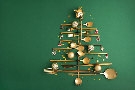 Golden cutlery arranging creative Christmas tree on green background