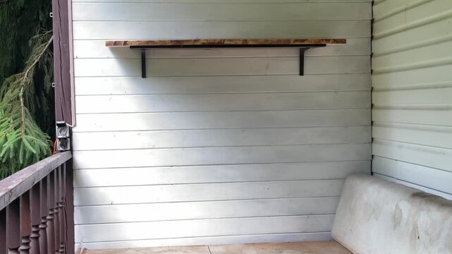 Empty outdoor sectional sofa on a rustic country house veranda before decoration and styling. Unfinished porch with worn cushions and a gray cat hiding beneath the wooden bench, capturing the "before"