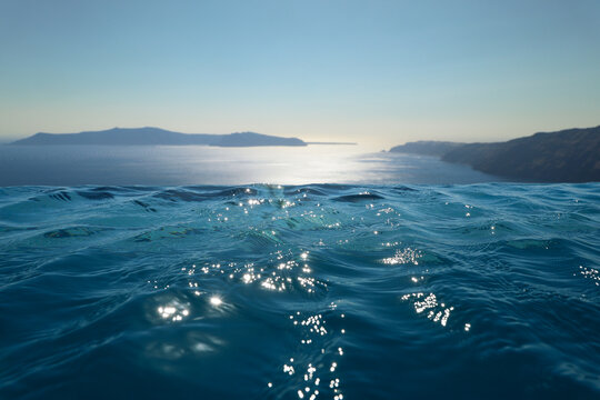 Infinity pool water merges seamlessly with the Aegean Sea as sunlight dances across gentle waves, framing Santorini&rsquo;s volcanic islands in a serene, dreamlike Mediterranean horizon.