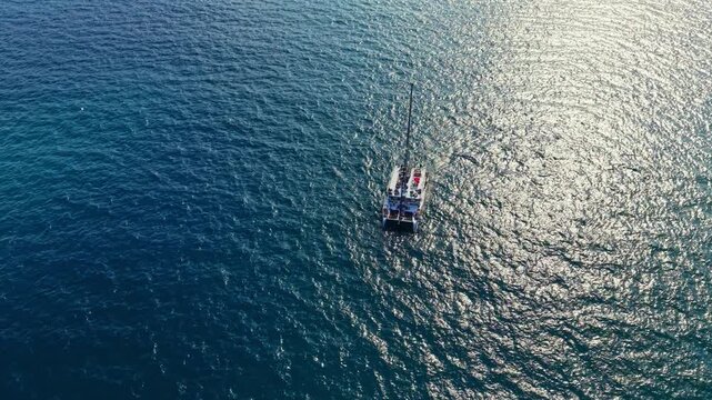 A small boat is seen on the water with bright sunlight shining down. The ocean water appears clear with light patterns reflecting on its surface.
