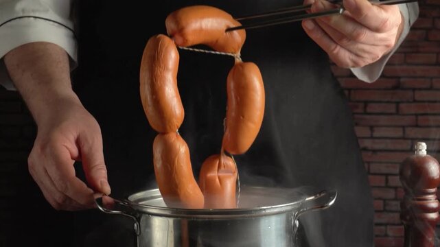 Chef using tongs to lift sausages from a steaming pot, showcasing the cooking process in a kitchen with a rustic brick wall background
