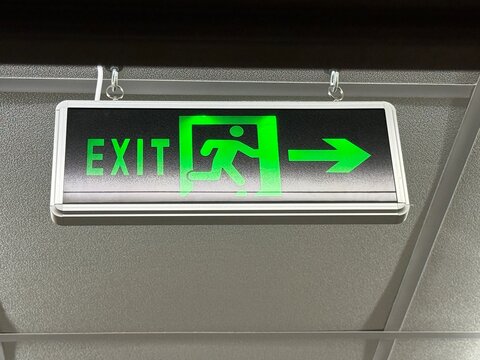 Exit sign hanging from ceiling with green arrow and running figure, suitable for emergency awareness