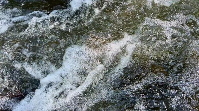 Extreme closeup of foamy river water surface with bubbles in sunlight