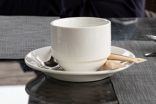 A white coffee cup on a saucer with a tablespoon and sugar on a glass table. A cozy coffee setting in a cafe or restaurant