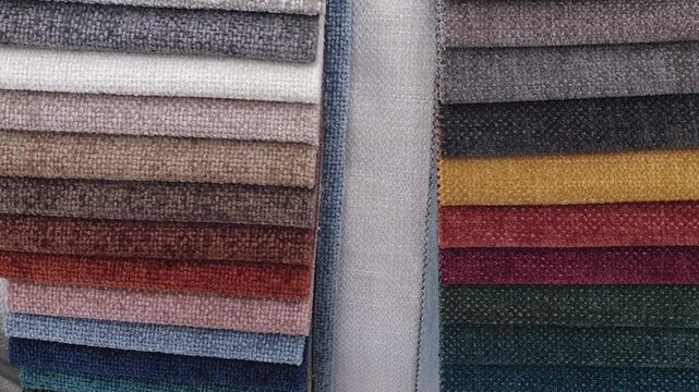 Slow motion panning shot across a colorful catalog of upholstery fabric swatches and textile material samples. Interior
