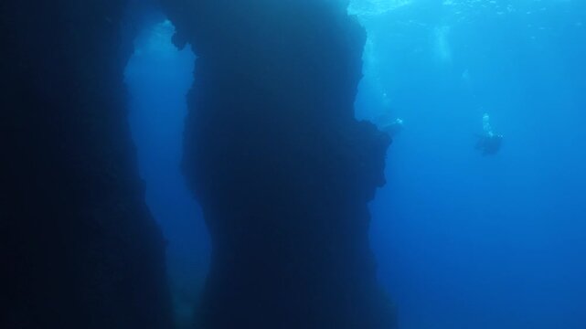 scuba divers exploring and swimming around an arc underwater cave and tunnel swim trough 