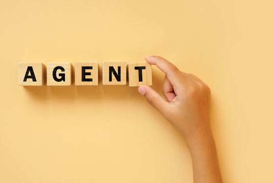 Hand arranging wooden letter blocks spelling AGENT on a bright background. Concept of artificial intelligence agents, automation, business services, representation and professional assistance.