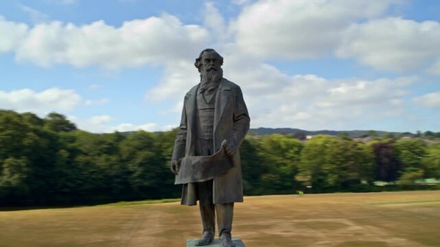 Aerial drone view orbiting the Sir Titus Salt statue in Roberts Park, Saltaire, on a sunny day