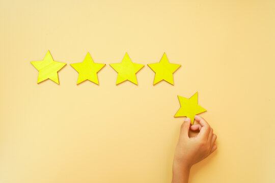 Hand placing a yellow star beside a row of yellow stars on a bright background. Concept of five star rating, customer satisfaction, excellent service, quality and positive reviews.