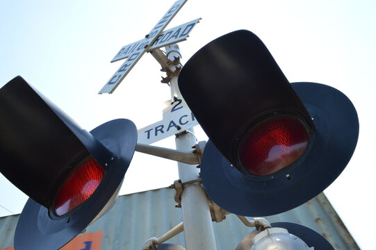 Low-angle close-up of railroad crossing warning lights and crossbuck sign against a bright sky for transportation, railway safety, trains, and infrastructure.