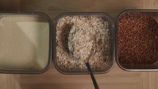 Scooping raw oatmeal flakes with a metal spoon from a box