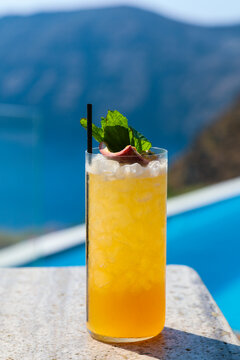 Golden mezcal cocktail glows beside a Santorini infinity pool, garnished with mint and passion fruit &mdash; a refreshing blend of island elegance, summer light, and Mediterranean leisure in every sip.