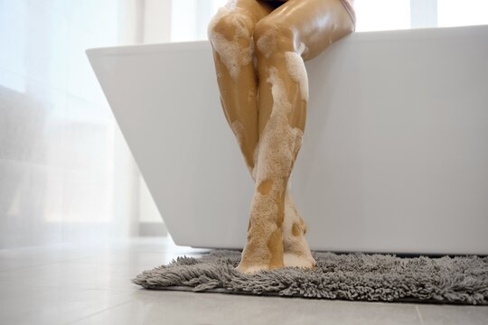 A person sits in a modern bathroom, enjoying a bubble bath. The white tub contrasts with the gray rug and the warm lighting, creating a calming atmosphere perfect for relaxation