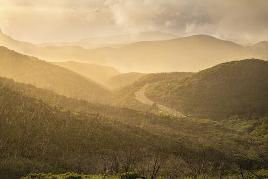 View from a path below the summit of Garajonay to other mountains of the Garajonay National Park and a road. Rain, sun and golden hour with bright clouds. Parque Nacional de Garajonay, La Gomera, Canary Islands, Spain