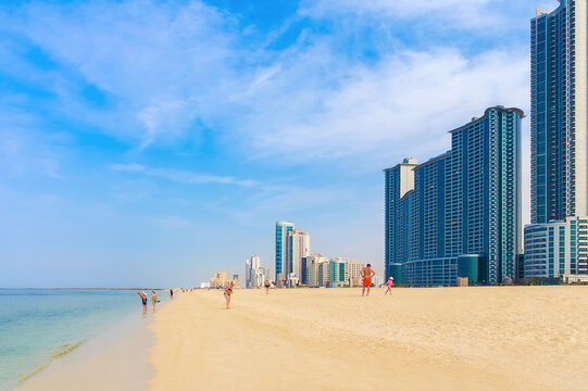 Modern high-rise skyscrapers and public beach in Ajman, UAE. Resort lifestyle concept, sunny summer day
