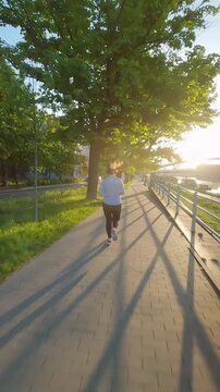 Caucasian woman runs along the embankment. Unusual view, filmed on FPV drone. 