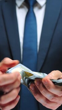 Formally dressed man is counting US Dollar bills, close-up.