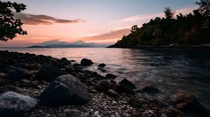 Obraz premium Sunset over calm sea with rocky shore and forested hillside under soft pink and orange sky