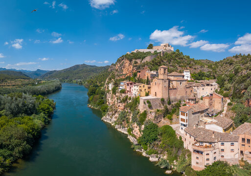 Panoramic view of Miravet village with its Templar castle perched on rocky cliffs above the Ebro River, surrounded by green hills and Mediterranean landscape, Tarragona, Catalonia