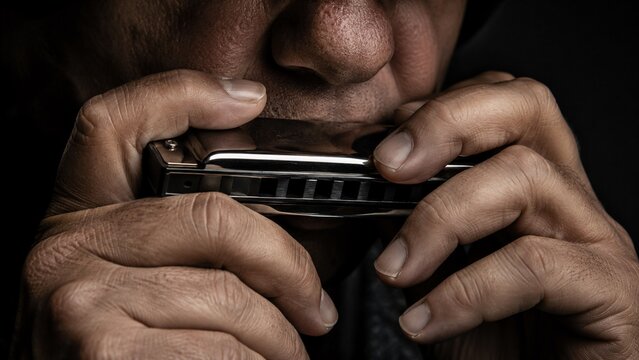 Close-up of a musician's hands and face playing the blues harmonica