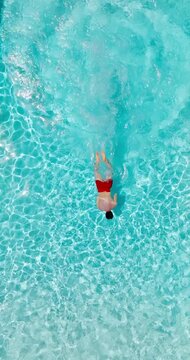 Aerial view as a man dives into the pool and swims. Slow motion