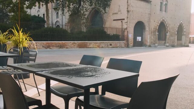 Outdoor cafe with tables and chairs on paved terrace in old town square in Rimini, Italy, with view of Castel Sismondo and historic Renaissance fortress. Italian piazza with sidewalk restaurant