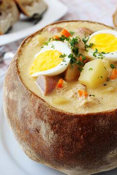 Polish sour rye soup with sausage, potatoes, carrots and a halved egg served in a bread bowl. Comfort food, traditional cuisine, rustic dining, hearty meal, cozy lunch, farmhouse cooking.