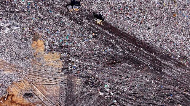 Overhead view of shredded waste texture, landfill. Colorful debris pattern with two bulldozers casting long shadows.