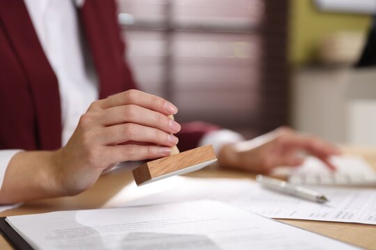 Woman stamping document while working on computer at desk indoors, closeup