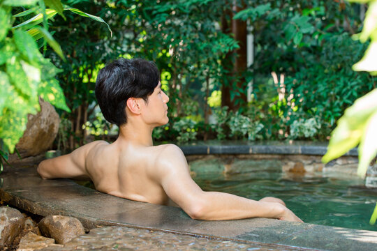 Man relaxing in outdoor hot spring bath surrounded by lush tropical garden
