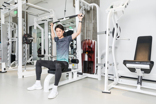 Young man training on lat pulldown machine in modern gym