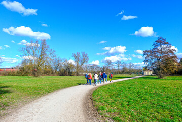 Obraz premium Gruppe von Wanderern mit Rucksäcken auf einem Spazierweg an einer großen Wiese im Frühling in Kahl am Main, Bayern