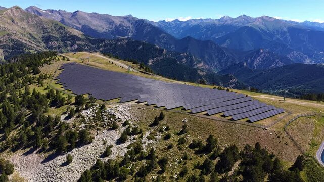 Aerial view of a large diamond-shaped photovoltaic solar farm on a high-altitude alpine slope in Andorra, surrounded by rocky terrain, pine forest, and sweeping Pyrenean mountain panorama