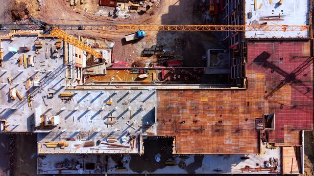 Rebar flooring at building site. Top down drone shot of construction materials, crane arm and a parked van on bare earth.