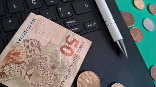 Brazilian fifty reais banknote and coins on laptop motion footage
