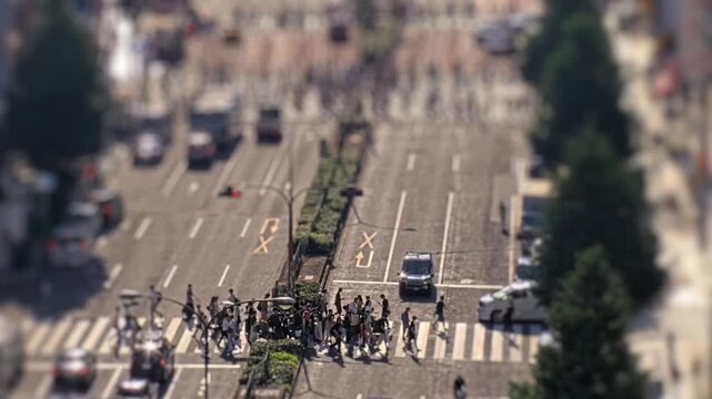 Tilt shift style timelapse of vehicles and pedestrians moving through a busy city intersection in Tokyo, Japan. High angle view with crosswalk activity and urban traffic flow.