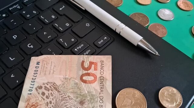 Brazilian currency bank note and coins resting on laptop motion clip