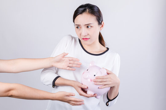 Worried woman protecting piggy bank from reaching hands