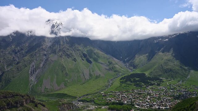 Majestic Mount Kazbek peak in clouds over Stepantsminda town landscape Caucasus Georgia. Epic alpine valley, wilderness nature, exploration hiking travel destination, travel concept. 