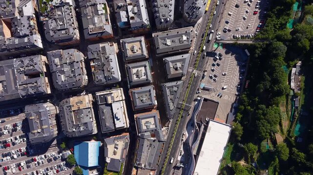 Overhead view of Andorra la Vella capital city showing dense urban blocks, rooftops, parking lots and main boulevard with traffic bordered by forested mountain slopes