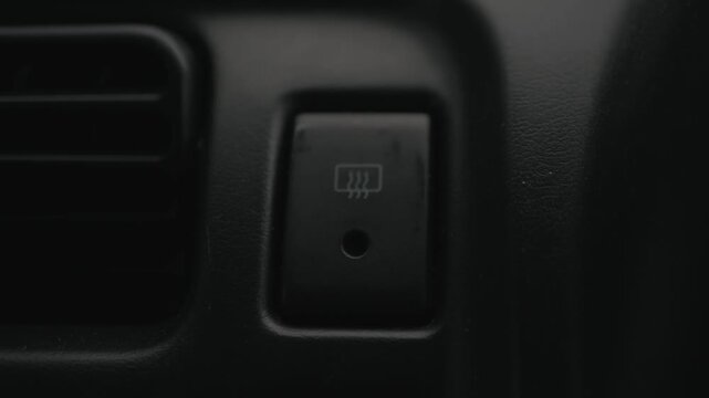 Close-up of fingers pressing the rear window defroster button to turn it off, symbolizing automotive climate control, visibility, and winter driving.