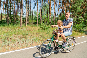 Fototapeta premium A young father carries his little daughter in a bicycle seat. Dad and child ride a bike in forest
