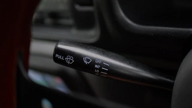Close-up of driver&rsquo;s hand adjusting the windshield wiper control stalk inside a car, highlighting vehicle operation, safety, and driving convenience.