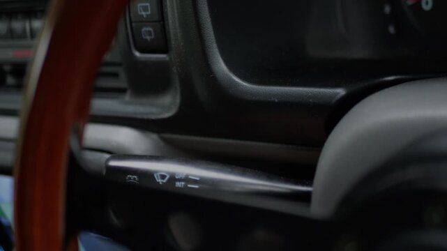 Close-up of driver adjusting windshield wiper control stalk inside a car, representing vehicle operation, safety, and driving convenience.