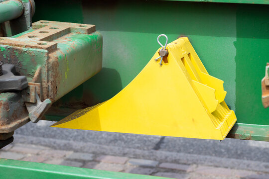 Yellow wheel chock secured to a green machinery component, positioned on a cobblestone surface, highlighting safety equipment in an industrial setting