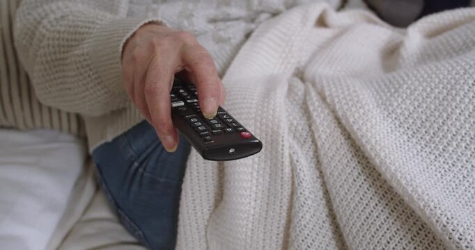 Person cozy on a sofa controlling the TV with a remote. Relaxing home scene.